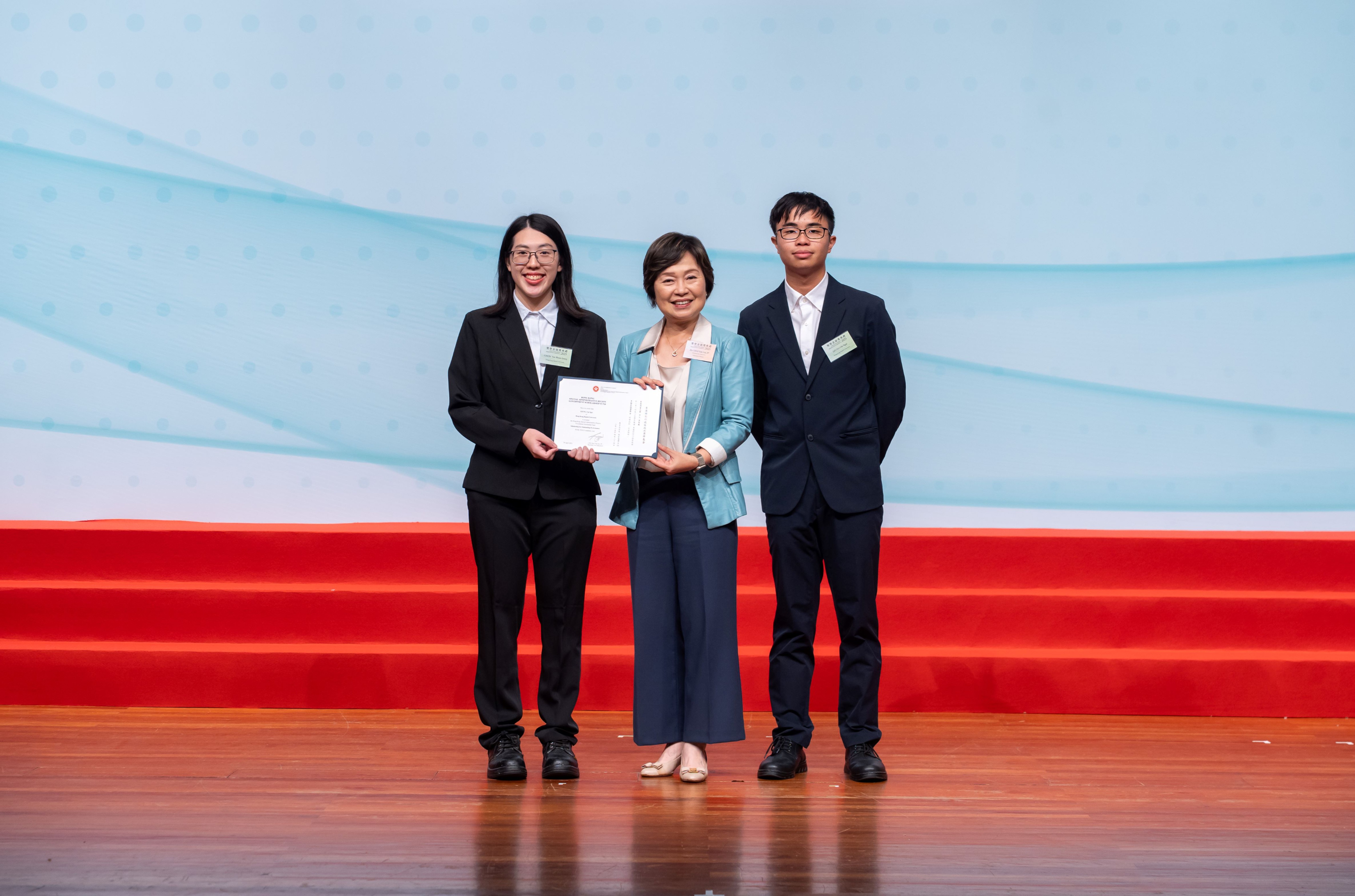 Dr. Yuk Lin CHOI (centre), Secretary for Education, presents the scholarship certificates to Yan Shuen CHOW, Jenny (left) recipient of the Endeavour Merit Award, and Chi Ngai LEUNG (right), recipient of the Scholarships for Outstanding Performance. 